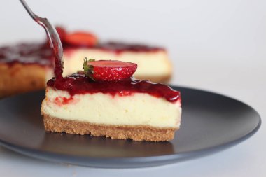 Bir dilim çilekli kek. Üstünde ev yapımı taze çilek sosu olan ipeksi yumuşak ve kremalı peynirli pasta. Beyaz arka planda taze çileklerle çekilmiş..