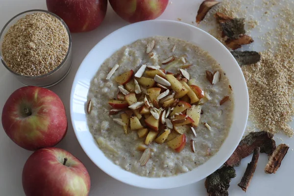 Broken wheat or Dalia porridge. Porridge for breakfast made with broken wheat and milk, served with cinnamon flavored caramalised apples and sliced almonds. Shot on white background