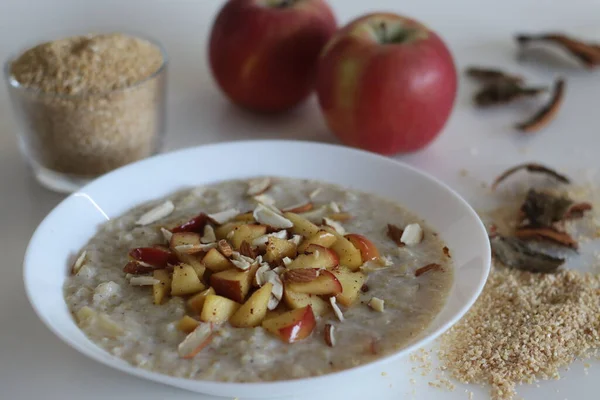 Broken wheat or Dalia porridge. Porridge for breakfast made with broken wheat and milk, served with cinnamon flavored caramalised apples and sliced almonds. Shot on white background