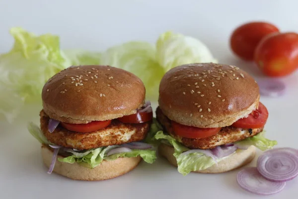Homemade cottage cheese burger. Paneer or cottage cheese patties, tomatoes, onions and lettuce placed inside homemade burger buns. Shot on white background.