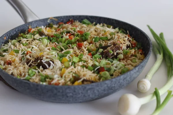 Meat rice vegetables in a pan. Cooked basmati rice tossed with sauteed vegetables and roasted mutton garnished with spring onions. Shot on white background.