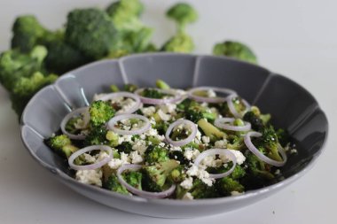 Peynirli brokoli ve soğan halkaları. Sotelenmiş brokoli çiçekleri üzerine buruşuk peynir ve soğan halkaları serpiştirilmiş. Yemeğe başlamak için sağlıklı bir yemek. Beyaz arkaplanda çekilen.