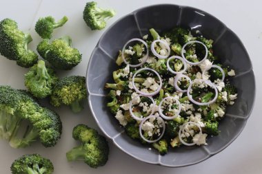 Peynirli brokoli ve soğan halkaları. Sotelenmiş brokoli çiçekleri üzerine buruşuk peynir ve soğan halkaları serpiştirilmiş. Yemeğe başlamak için sağlıklı bir yemek. Beyaz arkaplanda çekilen.