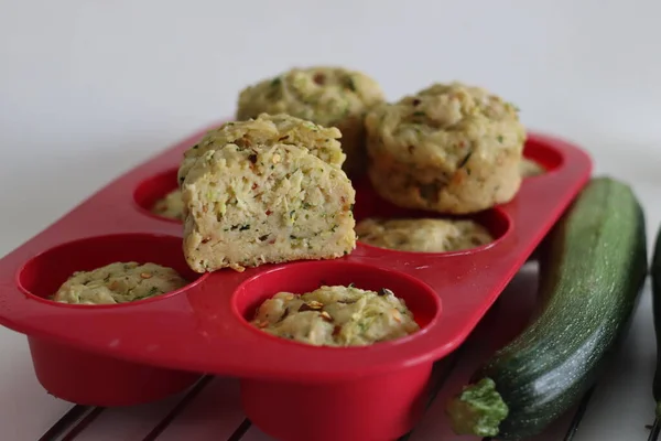 Cheese zucchini breakfast muffins. Savory breakfast muffins made of whole wheat flour, shredded zucchini, grated cheese and herbs. Shot on white background with muffins inside the red silicon mould.