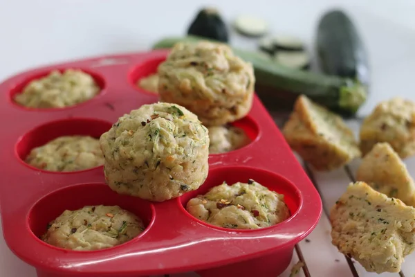 Cheese zucchini breakfast muffins. Savory breakfast muffins made of whole wheat flour, shredded zucchini, grated cheese and herbs. Shot on white background with muffins inside the red silicon mould.