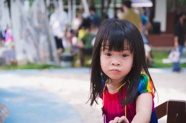 Yakından bakınca sevimli bir çocuk komik bir yüz ifadesi gösteriyor. Asyalı kız oyun alanında oynuyor. Yaz ya da bahar etkinlikleri.