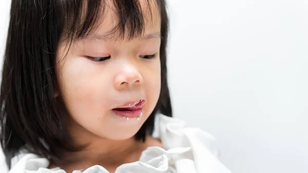 Cute child is licking the cream cake that follows her lips luscious.
