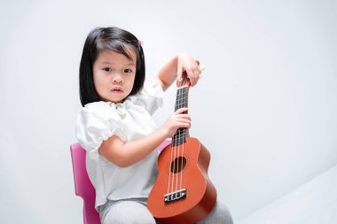 Asyalı kız uluslararası müzik eğitimi almaya hazırlanıyor. Kahverengi ukulele tutan çocuk.
