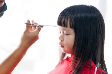 Yakın çekim çocuk yüzü. Berber el kâküllerini keserken çocuk oturuyor ve gözlerini kapıyor. Kız kendini kırmızı pelerine sarmış..