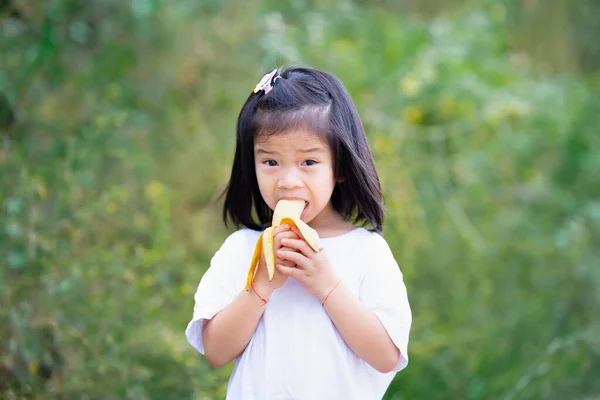 アジアの子供たちは果物をガストで食べる バナナを噛んだ子 緑の自然背景 スペースのコピー — ストック写真