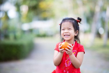 Happy child girl stands holding orange in her hand. Wealth luck. Chinese New Year concept. Empty space to enter text. Children laugh.
