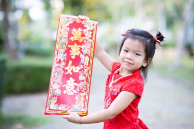 Cute 4 year old Asian kid girl holding red greeting placard with golden Chinese characters meaning Fulfillment. Chinese New Year concept.