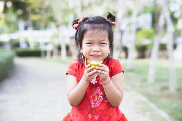 かわいい子供の女の子幸せな笑顔で伝統的な中国の金のインゴットを保持赤いChongsamを着て 中国の旧正月のコンセプト — ストック写真