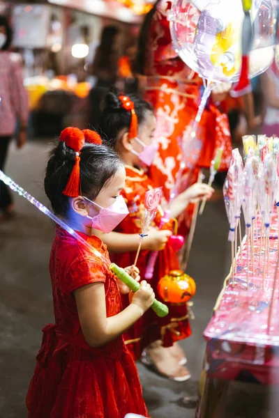 女儿和家人正在市场上的商店前购买糖棒棒糖 参观农历新年 人们穿着红色的旗袍 孩子们都戴着面具垂直图像 — 图库照片
