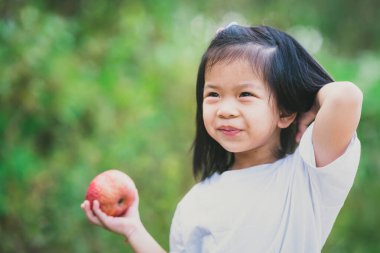 Asyalı şirin bir kızın portresi. 4 yaşında tatlı bir gülümseme. Elinde kırmızı elma meyvesi tutan mutlu çocuk. Metin girmek için boş alan. Doğa yiyecekleriyle sağlık.