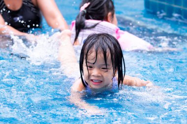 Aile tatillerde mavi yüzme havuzunda dinleniyor. Çocuklar suda oynarken eğlenirlerdi. Yetişkinler küçüklerin güvenliğiyle ilgilenirler. Mutlu gülümseyen çocuk 5 yaşında..