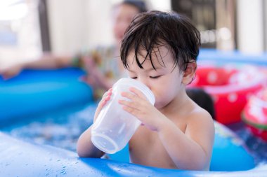 Portrait baby 1-2 years old. Asian child boy drinking water with plastic glass. Adorable kid standing in rubber pool. In summer time. Children drink water to quench his thirst and cool off heat.