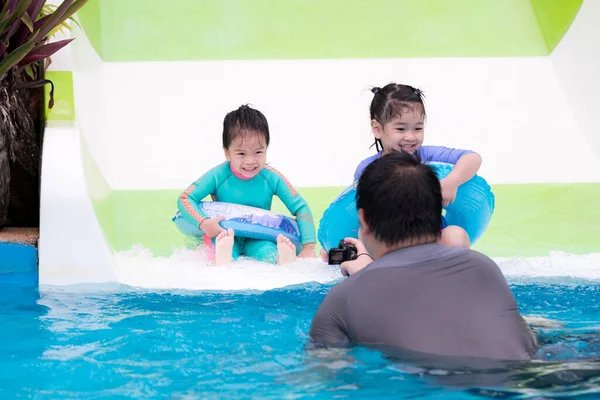 家庭假期的概念 两个女儿在游泳池里玩滑翔机 孩子们戴着橡皮圈 在他父亲身后 拿着小照相机的是拍摄视频 以捕捉快乐的回忆 肖像画儿童5岁 — 图库照片