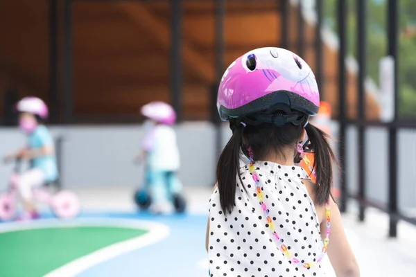 Rear back view. Children playing mini bike on playground street. Child are learning traffic signs and driving on road. Kid wearing pink helmet. Fun learn concept through play for good memory.