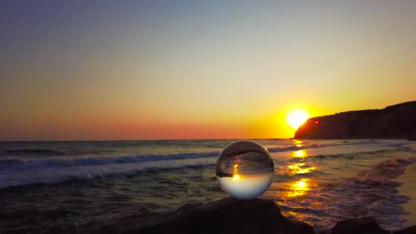 日落时分 一只玻璃球矗立在海边的悬崖上 而海水的喷射则缓缓喷涌而出 — 图库视频影像