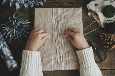 Eller el sanatları kağıdına sarılmış şık bir Noel hediyesi. Kırsal ahşap masa üzerinde iplikle mavi kağıt yıldızlar. Düz yatıyordu. Atmosferik karamsar görüntü, İskandinav tarzı. Mutlu Noeller ve mutlu tatiller!