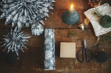 Yılbaşı hediyesini paketlemek kırsal bir düzlük. Basit bir hediye kutusu, makas, mum, mavi kağıt yıldızlar, ahşap masa süsleri. Atmosferik görüntü, kuzey tarzı. Tatil hazırlığı