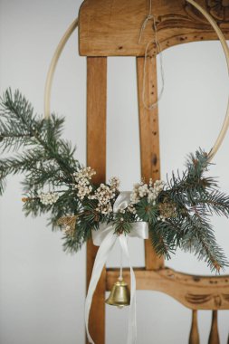 Kırsal ahşap sandalyede çan asılı modern noel çelengi. Kış tatili hazırlığı, atmosferik karamsar görüntü. İskandinav odasında şık bir boho xmas çelengi. Mutlu Noeller.!