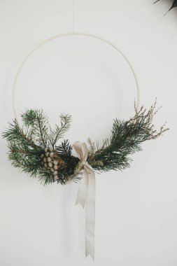 Beyaz arka planda asılı modern minimalist Noel çelengi. Mutlu Noeller ve mutlu Noeller! Köknar dallı Boho çelengi, esmer bitki, kurdele. Kış tatili hazırlığı