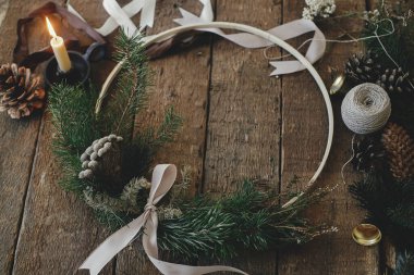 Kırsal ahşap arka planda modern noel çelengi. Kurdeleli, mumlu, iplikli, çam kozalaklı esmer bir çelenk. Atmosferik görüntü. Mutlu Noeller ve mutlu tatiller!