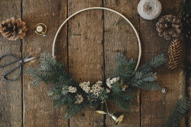 Modern noel çelengi, kırsal düzlük. Minimalist Xmas boho çelengi, çan, çam kozalakları, iplik, kırsal masada makas. Atmosferik karamsar görüntü. Mutlu Noeller.!