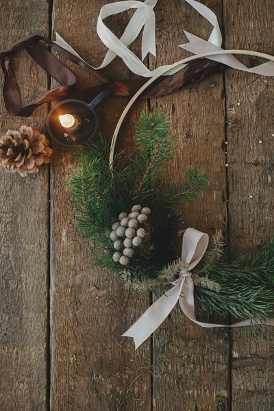 Modern christmas wreath flat lay on rustic wooden background. Boho wreath with brunia on rustic table with ribbons,candle, pine cones. Atmospheric image. Winter holiday preparation