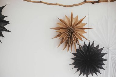 Beyaz duvardaki ahşap dalda asılı şık Noel yıldızları. Modern İskandinav şenliği dekoru. Basit bir İsveç zanaatı, siyah beyaz kağıt yıldızlar. Kış tatili hazırlığı.