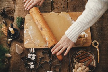 Geleneksel Noel kurabiyeleri için, elleri ahşap oklavayla zencefilli ekmek hamuru yuvarlıyor. Kırsal masada metal kesiciler, baharatlar, dekorasyonlarla zencefilli kurabiye yapmak.