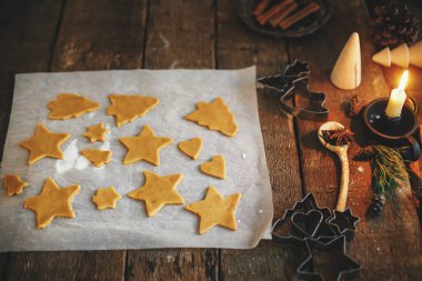 Kırsal masada geleneksel zencefilli kurabiye yapıyorum. Noel yıldızında zencefilli çörekler ve mum, baharat ve süslemelerle kabartma kağıdı üzerinde ağaç şekilleri. Huysuz resim