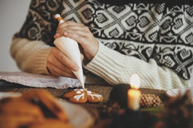 Noel kurabiyeli zencefilli ren geyiklerini mum, baharat ve dekorasyonla süsleyen eller. Atmosferik karamsar görüntü. Geleneksel zencefilli kurabiye yapan kadın