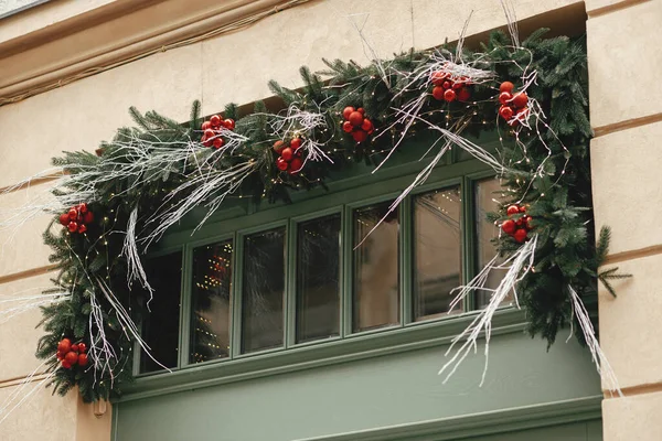 ヨーロッパの街の通りでドアや窓にスタイリッシュなトウヒの枝や赤い竹の装飾 冬の休日のための建物の現代のクリスマスのお祝いの装飾 メリークリスマス — ストック写真