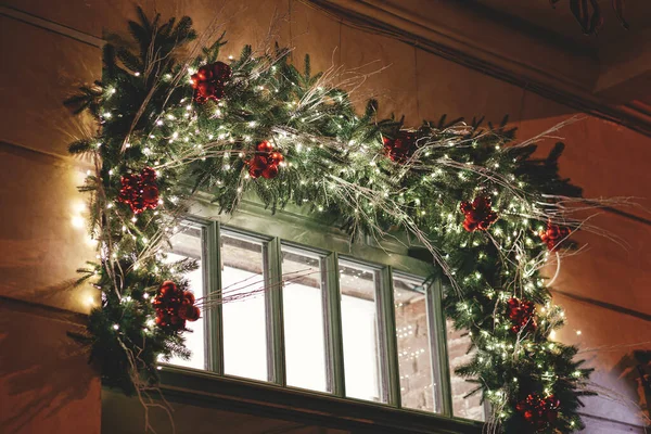 夕方には建物の窓に照明の装飾が施されたスタイリッシュなクリスマススプルースの枝 大気魔法の時間だ 冬の休日のクリスマスのお祝いの装飾 メリークリスマス — ストック写真