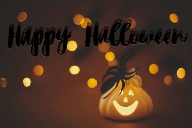 Işıldayan Jack o fener kabağı üzerine Cadılar Bayramı mesajınız kutlu olsun. Turuncu arka planda örümcekli, ışıklı ve uçan siyah yarasalı. Sezonun tebrik kartı. El yazısıyla mutlu Cadılar Bayramı metni