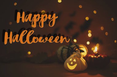 Balkabağı üzerine Cadılar Bayramı mesajınız kutlu olsun, parlayan Jack O feneri, mum, koyu turuncu arka planda ışıklı örümcek ve uçan siyah yarasalar. Sezonun tebrik kartı. El yazısıyla mutlu Cadılar Bayramı metni