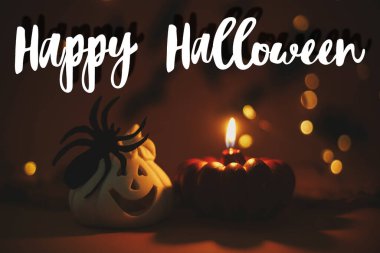 Cadılar Bayramı 'nda balkabağı mumu ve koyu turuncu arka planda örümcekli ve uçan siyah yarasalı Jack O feneri üzerine mutlu mesajlar. Sezonun tebrik kartı. El yazısıyla mutlu Cadılar Bayramı metni