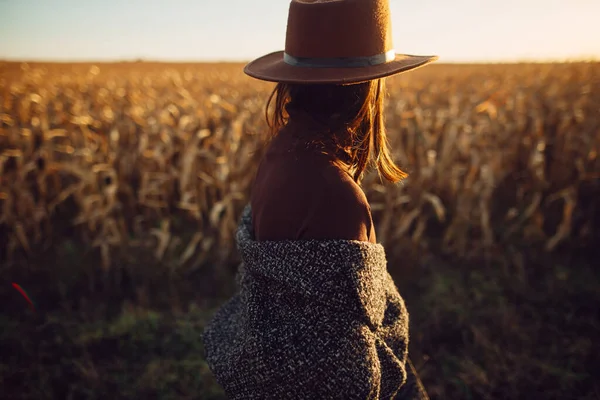 秋のフィールドで日没の光の中を歩く帽子の美しいスタイリッシュな女性 大気中の瞬間 田舎のトウモロコシ畑で夜を楽しむレトロな衣装のファッショナブルな若いヒップスター女性 — ストック写真