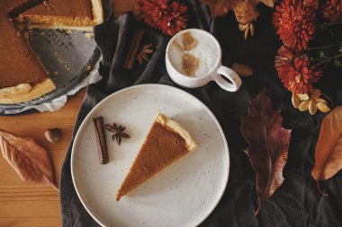 Modern tabakta balkabağı dilimi ve kırsal masada keten peçeteli sıcak kahve, sonbahar çiçekleri ve yapraklar, anason ve tarçın. Ev yapımı kabaklı tart tarifi. Üst Manzara. Mutlu Şükran Günleri