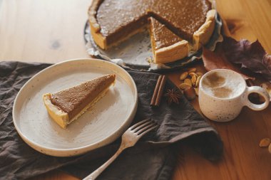 Mutlu Şükran Günleri Modern tabakta balkabağı dilimi ve kırsal masada keten peçeteli sıcak kahve, sonbahar yaprakları, anason ve tarçın. Ev yapımı kabak tartı tarifi..