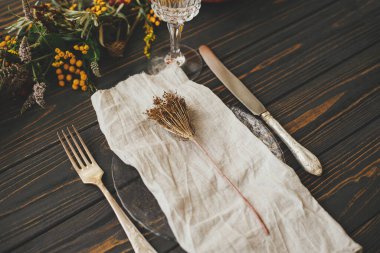 Şükran Günü yemeği kırsal masa hazırlığı. Klasik çatal bıçaklı modern tabak, keten peçete, ahşap masa üzerinde balkabağı ve sonbahar çiçekleri aranjmanı. Çevre dostu çiftlik evi Sonbaharda yemek servisi