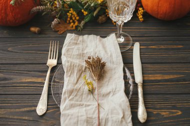 Klasik çatal bıçaklı modern tabak, keten peçete, ahşap masa üzerinde balkabağı ve sonbahar çiçekleri aranjmanı. Çiftlik evi kırsal sonbahar düğünü. Çevre dostu Şükran Günü sofrası.
