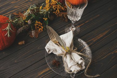 Şükran Günü yemeği kırsal masa hazırlığı. Klasik çatal bıçak takımı, keten peçete, ahşap masa üzerinde bitki ve cam, balkabağı ve sonbahar çiçek aranjmanı ile modern tabak. Çevre dostu yemek servisi.