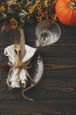 Şükran Günü yemeği kırsal masa hazırlığı. Klasik çatal bıçak takımı, keten peçete, ahşap masa üzerinde bitki ve cam, balkabağı ve sonbahar çiçek aranjmanı ile modern tabak. Çevre dostu yemek servisi.