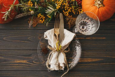 Klasik çatal bıçak takımı, keten peçete, ahşap masa üzerinde bitki ve cam, balkabağı ve sonbahar çiçek aranjmanı ile modern tabak. Köylü çiftlik evi düğünü. Şükran Günü sofrası.