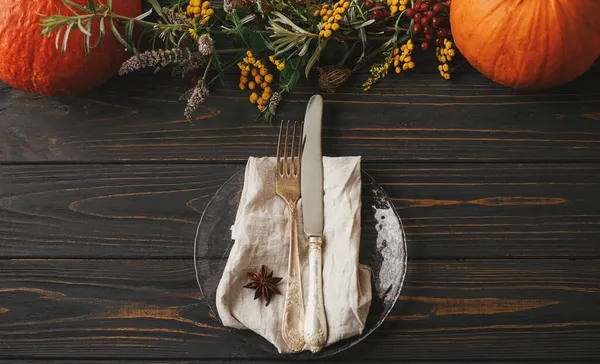 Şık bir Şükran Günü sofrası. Klasik çatal bıçaklı modern tabak, anason kaplı keten peçete balkabaklı ahşap masa ve sonbahar çiçekleri süslemesi. Çiftlik evi kırsal sonbahar düğünü