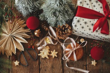 Atmosferik stil Noel kompozisyonu düzdü. Noel kurabiyeleri, hediye, kırsal ahşap masa üzerindeki şenlikli süslemeler. Xmas hediyesi, sağlıklı yulaf ezmeli kurabiyeler, süsler. Tatil karamsar görüntüsü